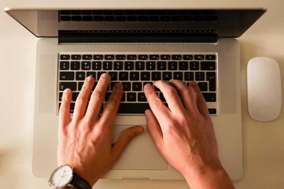 Overhead view of two hands typing on a laptop keyboard, with a mouse beside it