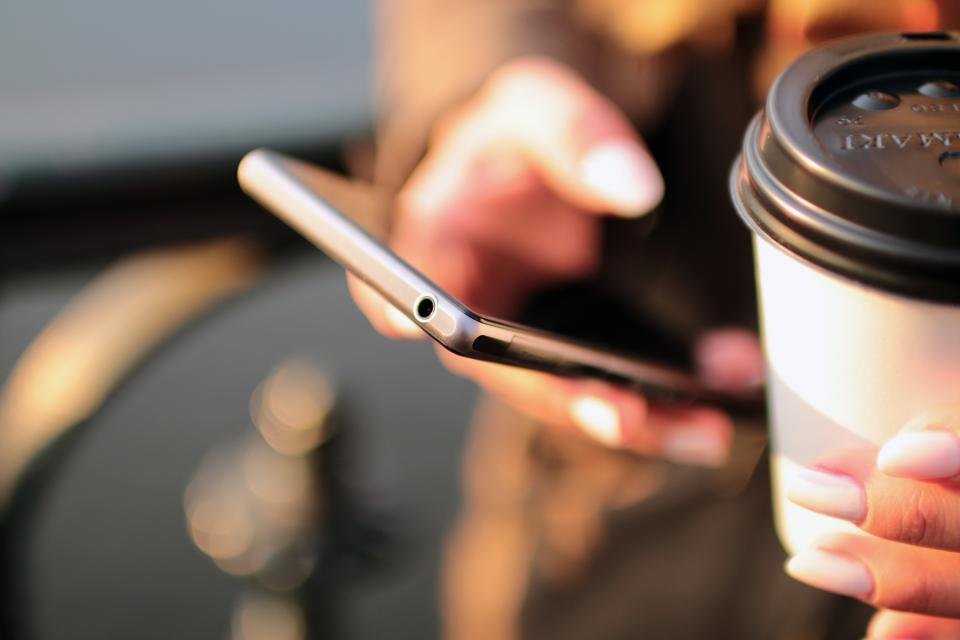 A hand holding a smartphone, with a paper coffee cup in the other hand
