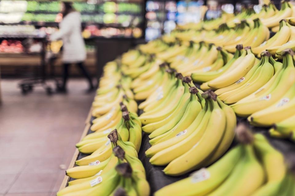 Rows of bananas in a supermarket, with a blurred shopper pushing a cart in the background